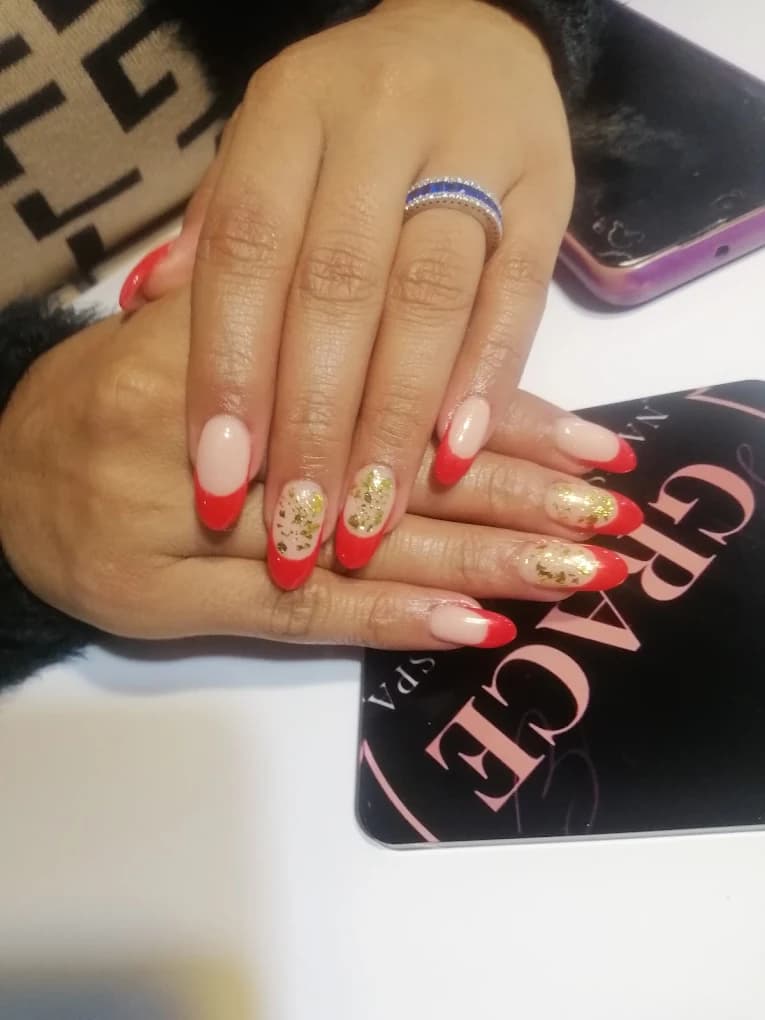 Almond nails with red french tips and gold foil flecks on two accent nails.